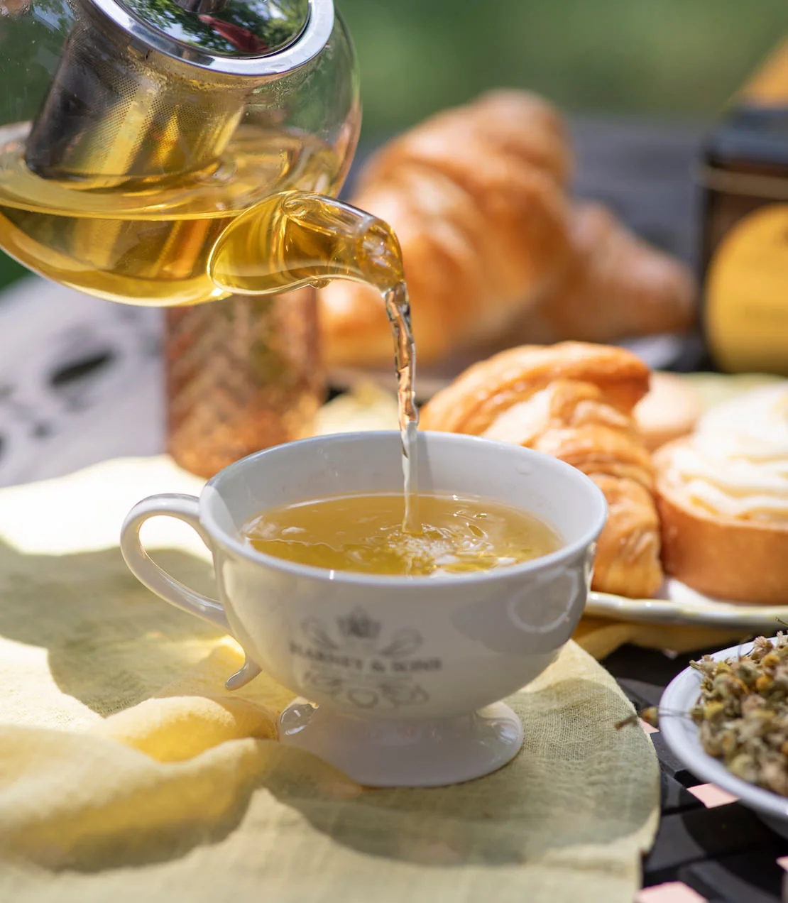 Golden chamomile infusion poured from a glass pot into a floral teacup
