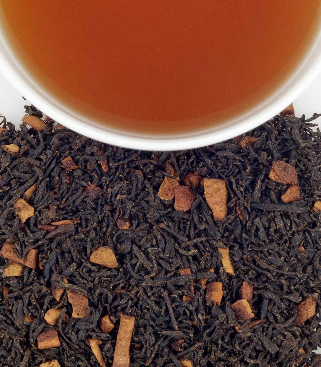 Brewed Harney & Sons Hot Cinnamon Spice tea beside loose black tea, cinnamon pieces and orange peel