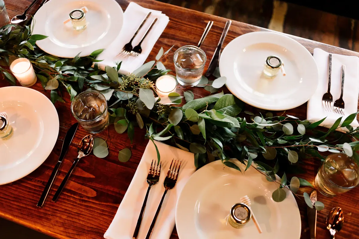 Dinner table with plates, cutlery, candles and greenery