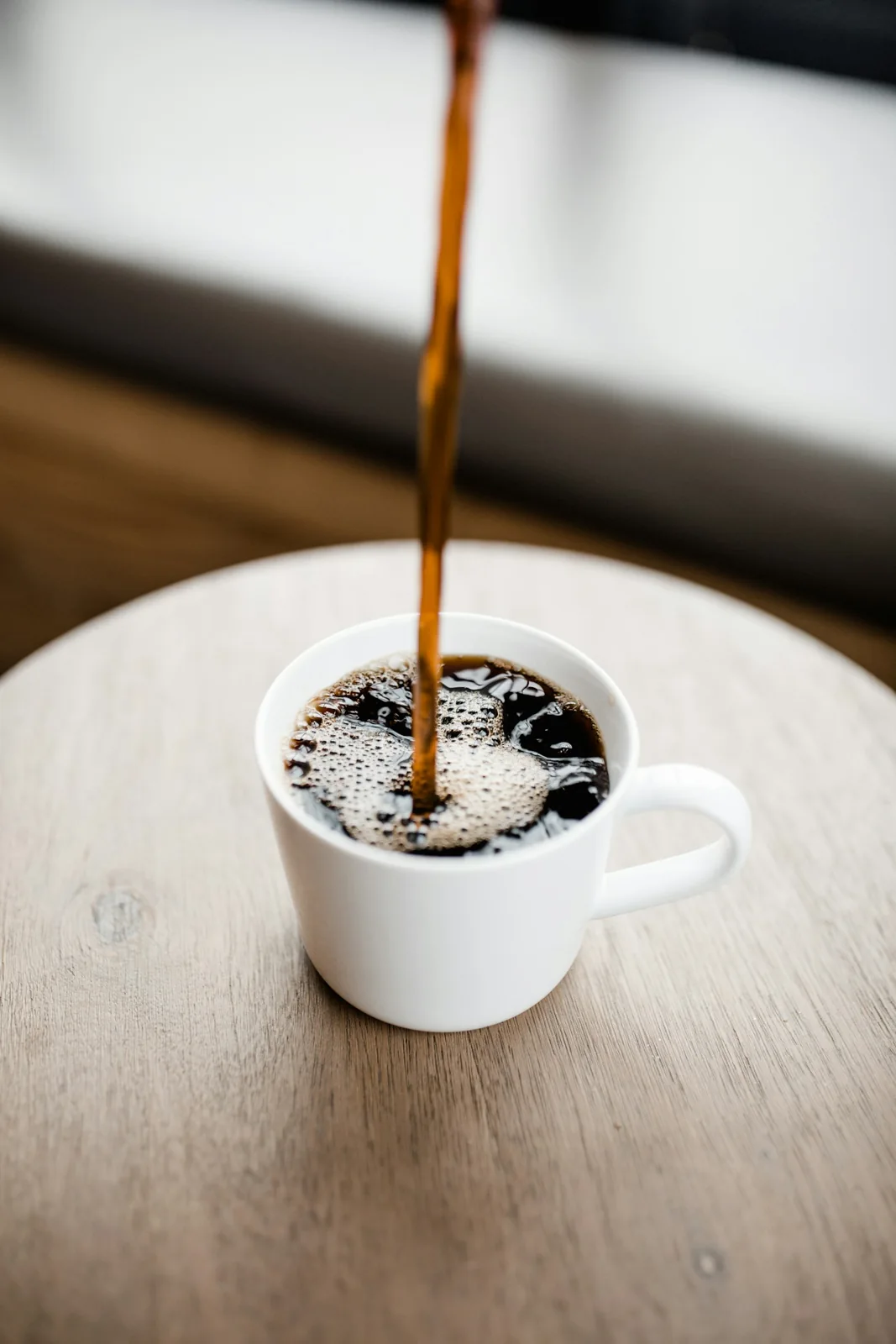 Coffee being poured into a white ceramic cup on a wooden table