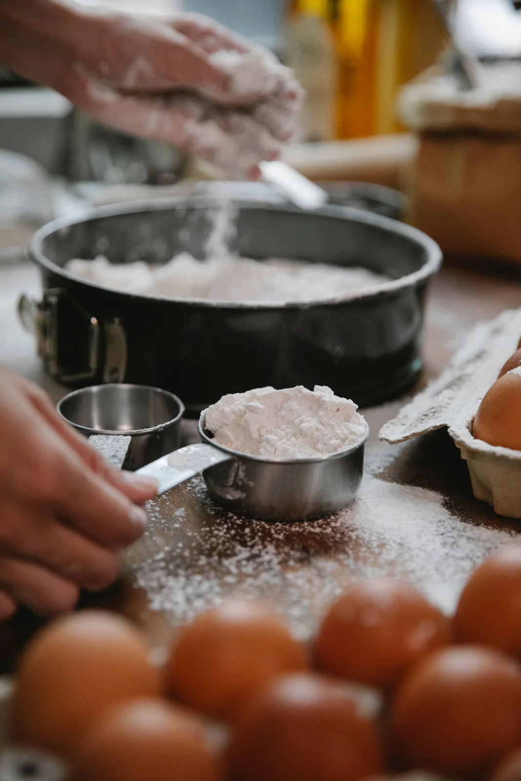 Flour being measured in a cup beside a baking pan