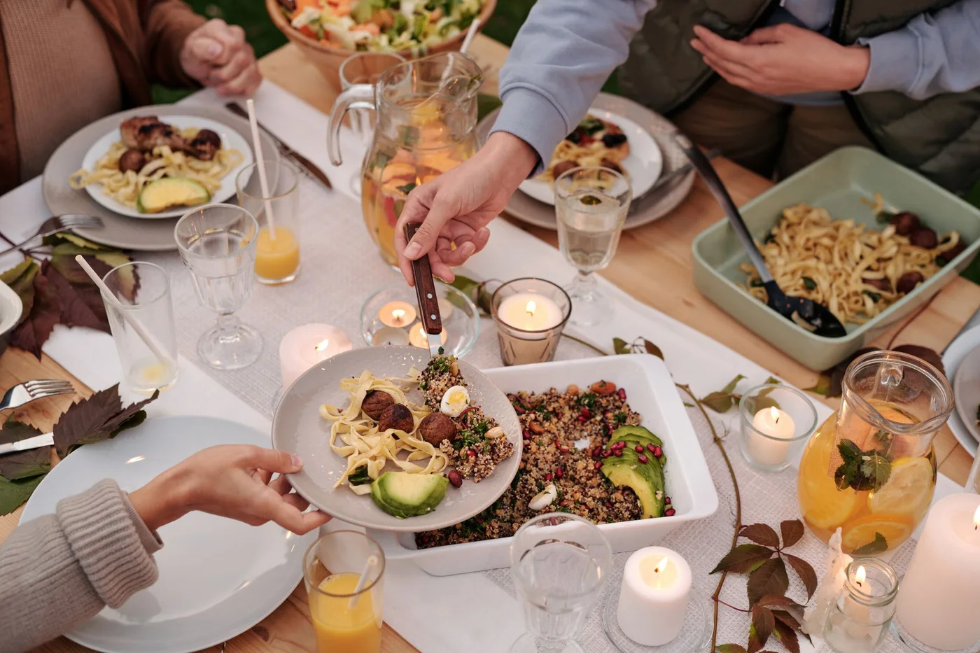 Friends sharing pasta, salad and drinks around a candlelit dinner table.