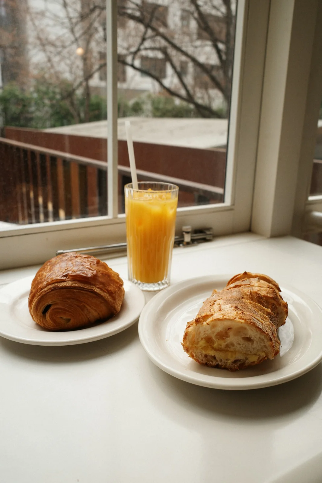 Pastries and orange juice on a table beside a window