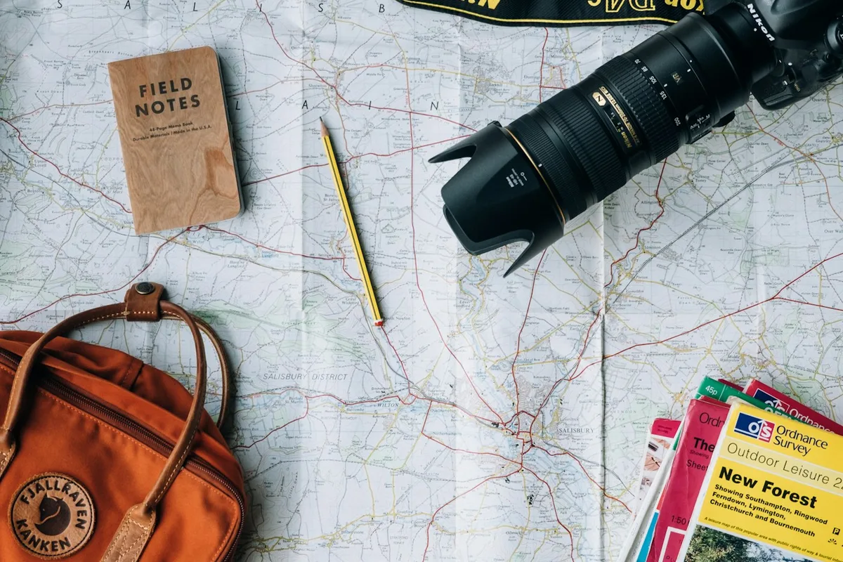 Map, notebook, camera, and travel bag arranged for planning.