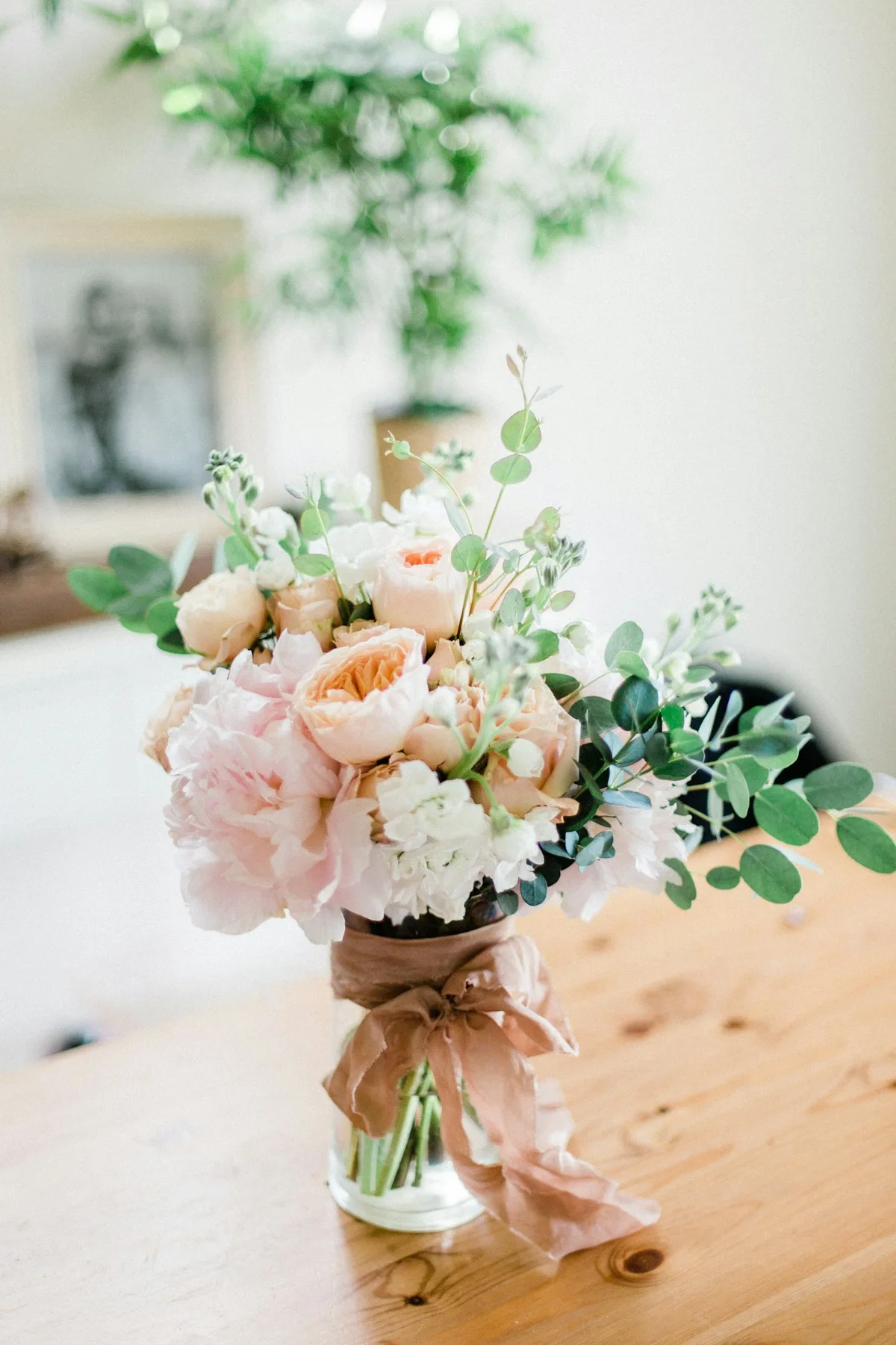 Pale flowers and foliage in a clear vase on a wooden table.