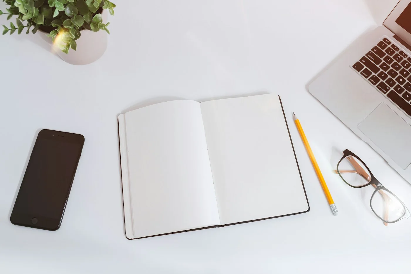 Open notebook, pens, glasses, and devices on a desk.