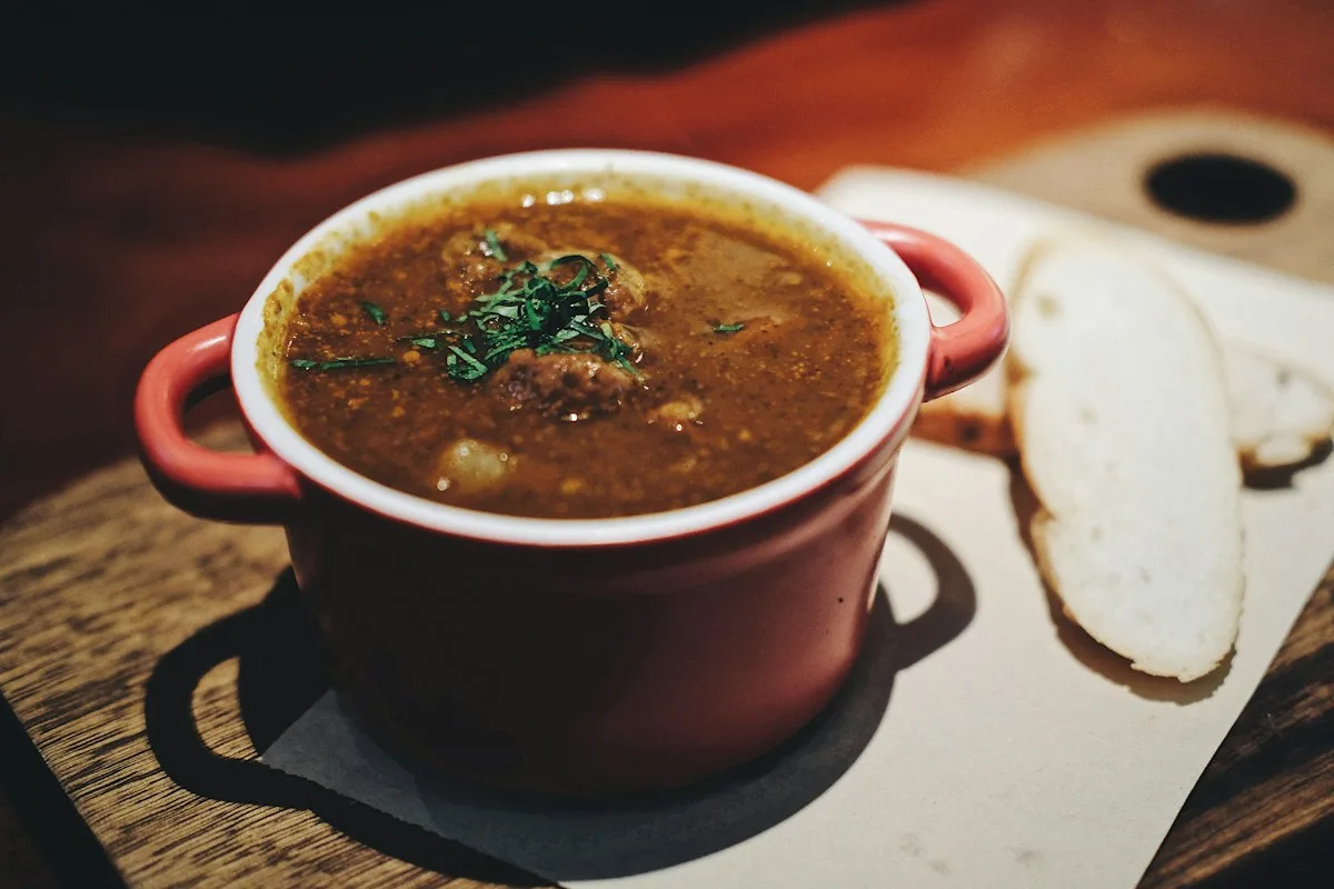 A red-handled bowl of soup beside sliced bread.