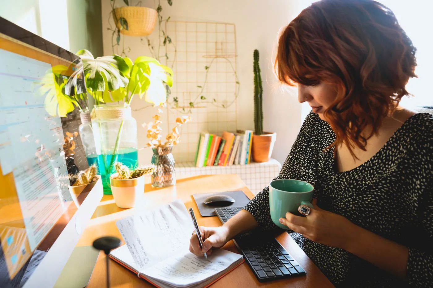 Woman writing at a home desk while holding a cup