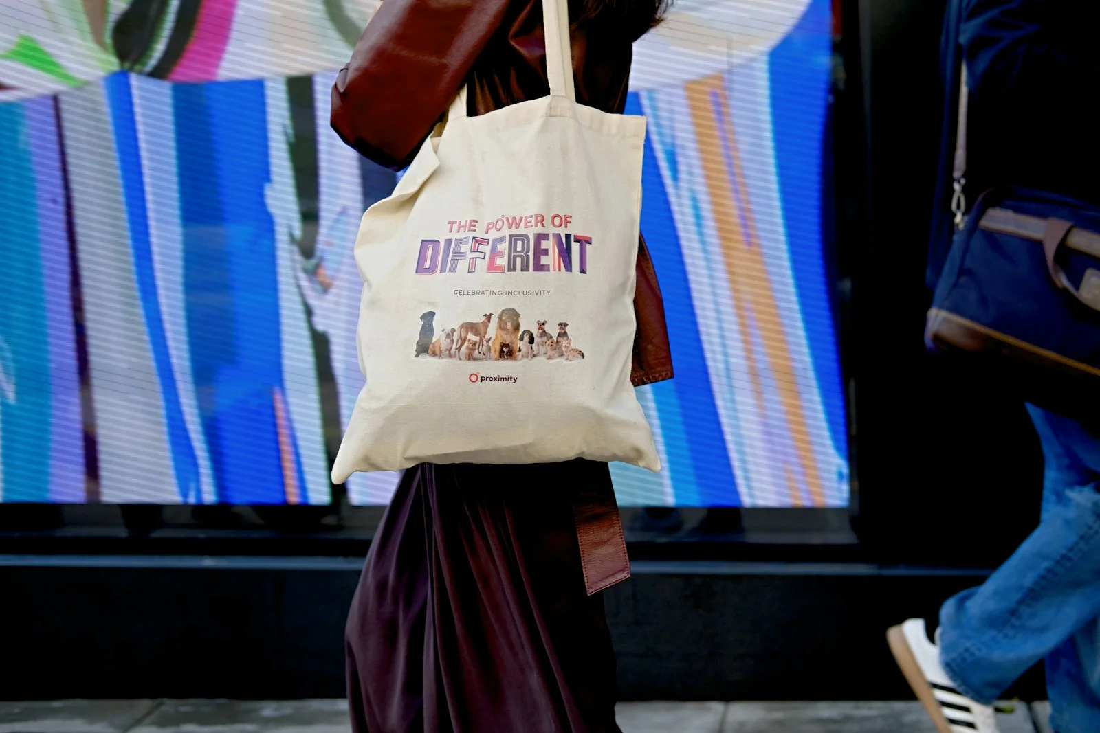 Person carrying a pale tote bag near a shopfront